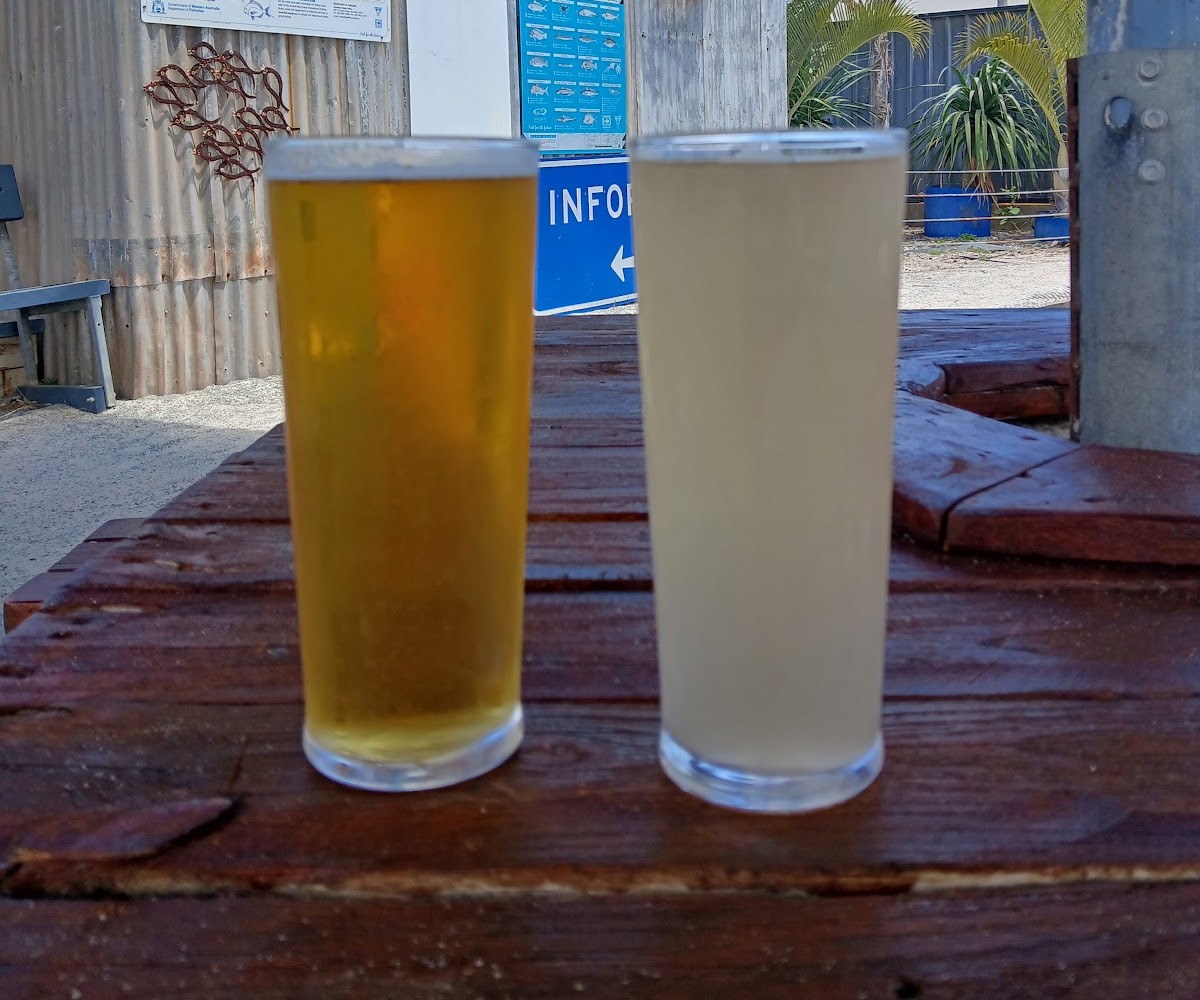 A pint of lager and a ginger beer side by side on a timber table in the sun